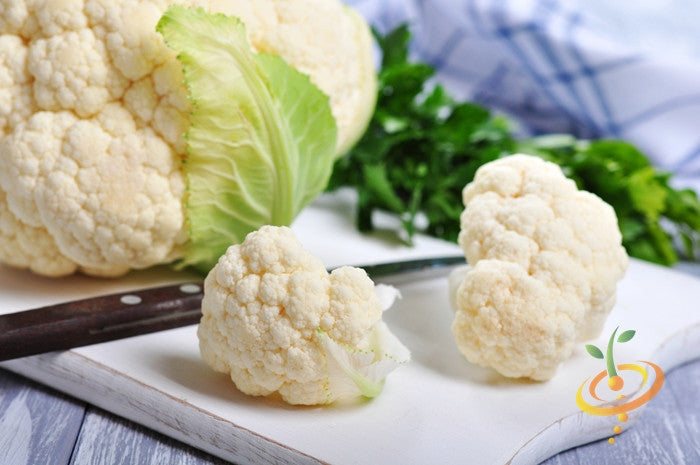 Fresh white snowball cauliflower florets on a cutting board with green leaves in the background