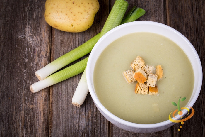 Creamy leek soup with croutons beside fresh leeks and a potato on wooden surface