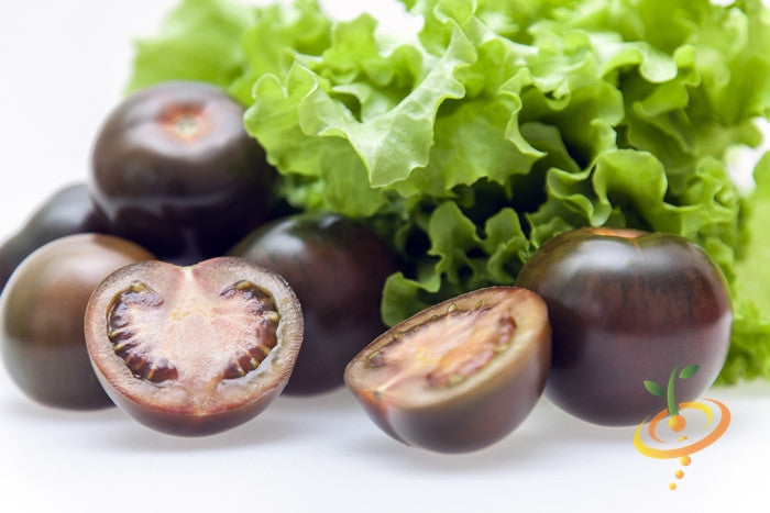 Close-up of black cherry tomatoes, whole and halved, with green lettuce leaves in the background.