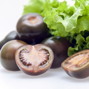 Close-up of whole and halved Black Cherry Tomatoes with green lettuce leaves in the background